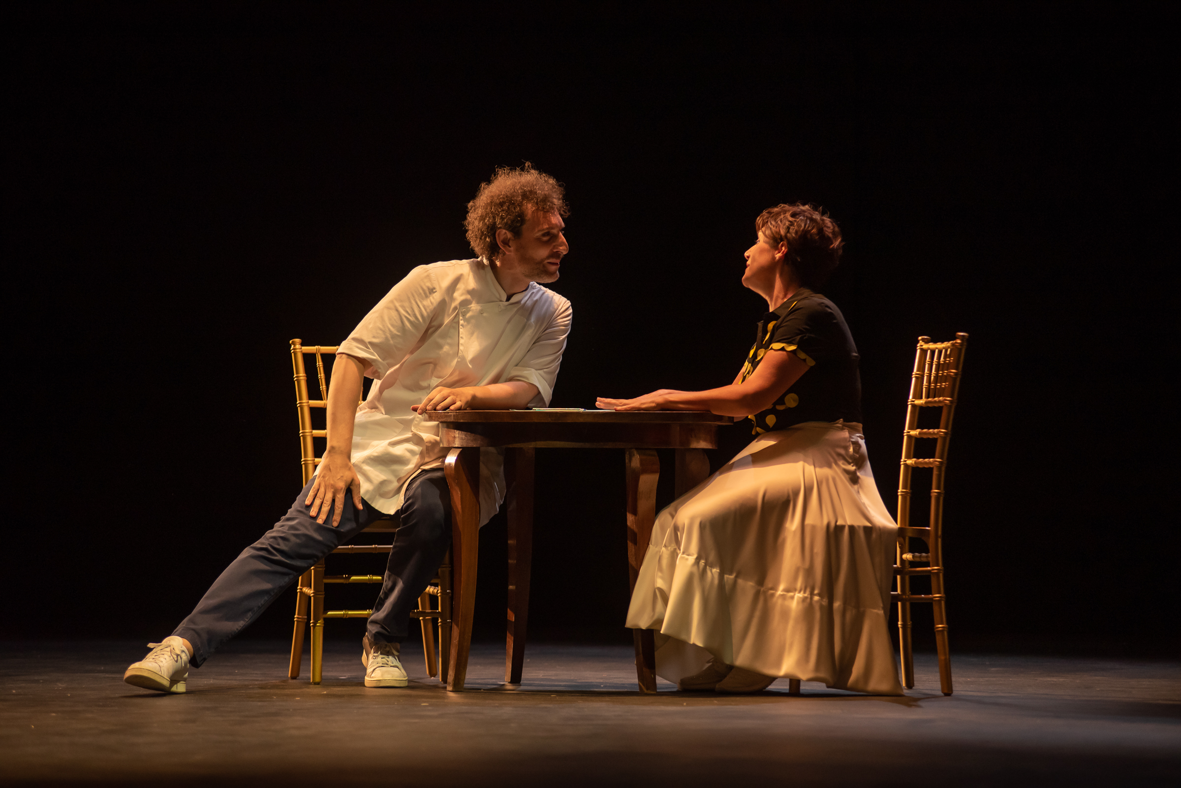 Seduti a un tavolo rotondo, Figaro (a sinistra) e Rosina (a destra) parlano sorridendosi
